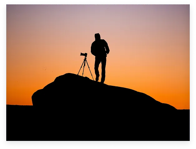 An astrophotographer and telescope silhouetted at sunset