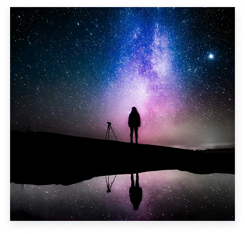 A photographer reflected beneath a colorful night sky
